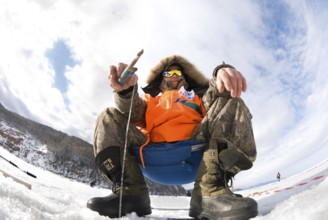 UST-BARGUZIN, RUSSIA - APRIL 11: A fisher sits with a rod at an ice hole during the 5th Annual