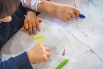 Two kids coloring drawings of animals with wax crayons, developing their creativity and fine motor