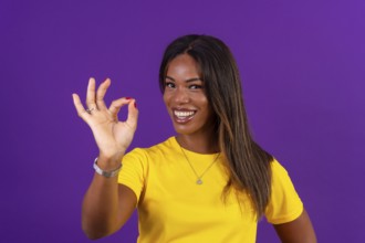 Studio portrait with purple background of an african smiling urban woman gesturing agreement with