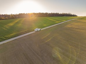 A car drives on a road through a rural landscape at sunset, Tesla new Model Y Juniper, Nagold,