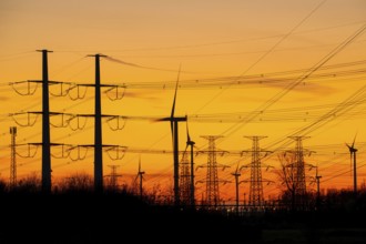High-voltage electricity pylons, transmission towers and wind turbines at sunset near the Borssele