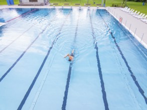 A swimmer moves in an almost empty swimming pool with clear lanes, Calw outdoor pool, Black Forest,