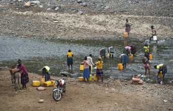 Women with plastic jerrycans fetching water and washing their bodies at a river near the road from