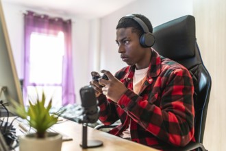 Young man focusing intently on playing video games while streaming live from a well equipped home