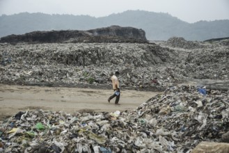 A person walking between garbage heap at a garbage dumpsite in the eve of World Environment Day, in