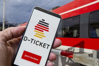 (Photomontage) Logo of the Deutschlandticket on a smartphone in front of a passing local train