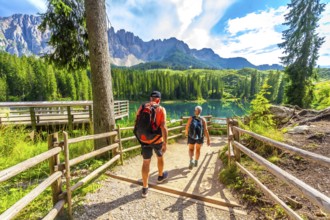 Tourists walking on a path towards the turquoise waters of lake carezza, surrounded by the stunning
