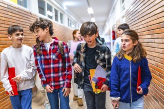 Elementary school students carrying backpacks and notebooks walk and chat together in school