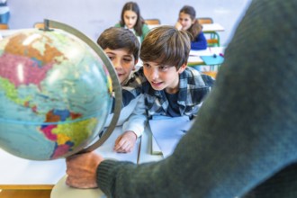 Curious elementary school students learning geography by observing a globe held by their teacher