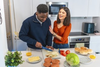 Cheerful multiethnic couple having fun while preparing burgers for dinner in their modern kitchen