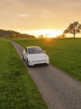 A white car drives along a small rural road at sunset, Tesla New Model Y, Germany
