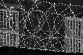 View through multiple coiled NATO wire onto the barred windows of Giessen Prison, Hesse, Germany