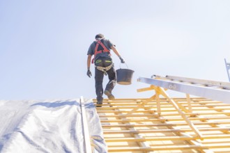 A worker in safety clothing climbs a ladder to work on a roof, in sunny weather, roof renovation,