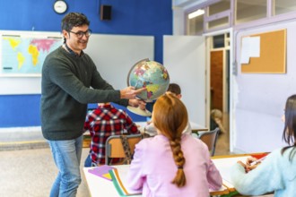 Geography teacher pointing a location on the globe to a classroom of elementary school students