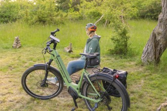 Cyclist with helmet sitting next to a bicycle, surrounded by green nature and trees, e-bike