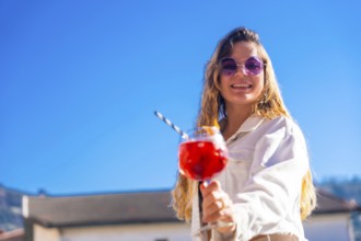 Chic blonde woman toasting with the camera holding a red cocktail in a rooftop in summer