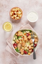 Caesar salad with salmon, with croutons and dressing, in a salad bowl, on a pink table