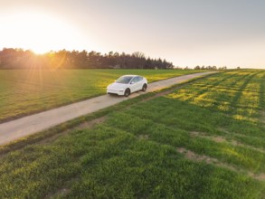 White electric car driving through a wide landscape on a country road at sunrise, Tesla New Model
