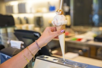 Womans hand adorned with bracelets, holding a delicious ice cream cone topped with crunchy nuts,