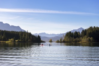 Two kayaks on a calm lake, framed by mountains and dense forests under a clear blue sky,