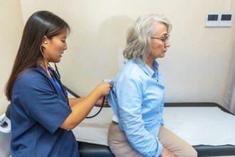 Female doctor examining the lungs of a senior woman with a stethoscope during a routine medical