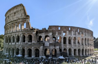 Side view of the Colosseum with tourists visible and sunlight illuminating its arches. Rome, Italy