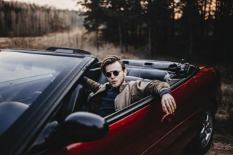 Man in a red convertible during sunset, exuding calm and confidence