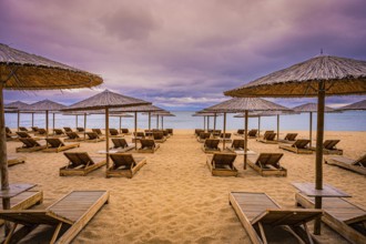 Deserted beach with bamboo umbrellas and sunbeds under a cloudy sky and calm sea, Golden Sands,