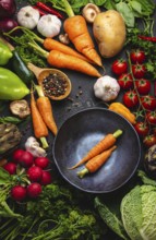 Two fresh farm carrots in vintage bowl and assorted organic vegetables on rustic black concrete