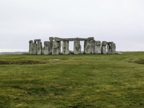 Distant view of Stonehenge surrounded by green grass under an overcast sky. Salisbury, England,