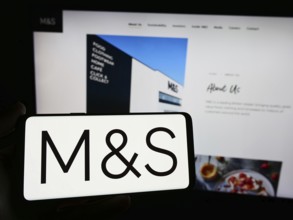 Stuttgart, Germany, 03-18-2024: Person holding smartphone with logo of British retail company Marks