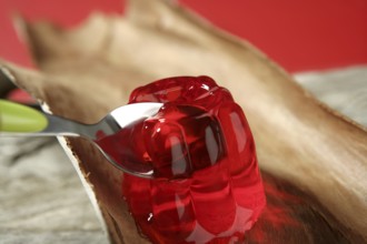 Jelly in red strawberry color in green spoon over wood