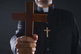 Priest holding cross of wood praying in foreground