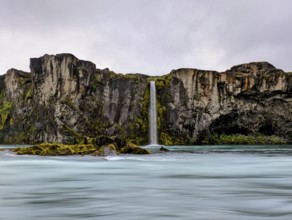 Vibrant waterfall cascading down moss-covered cliffs under a cloudy sky, Icelandic scenery. Iceland