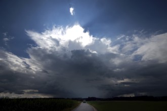 A lorry drives on a small country road directly towards a threatening thundercloud, doomsday