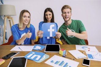 Smiling woman holding facebook logo with his friends showing thumbup sign