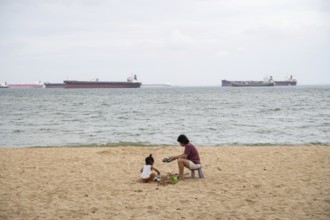 31.07.2023, Singapore, Republic of Singapore, Asia, A woman and a small child sit in the sand on