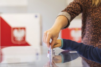 Woman's and kid's hands puting a card with a vote to the ballot box during parliamentary elections.