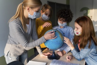 Female teacher with medical mask teaching geography with earth globe class