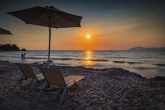 Beach scene with sunset, deckchairs and parasol in warm colours, Mastichari, Kos Island, Greece