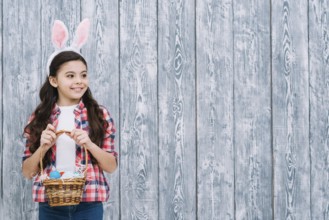 Portrait girl with bunny ears holding easter eggs basket looking away