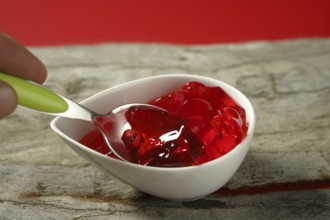 Jelly in red strawberry color in green spoon over wood