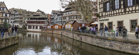 Panoramic photo of the river Ill with strolling tourists, surrounded by half-timbered houses in the