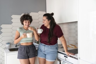 A lesbian couple stands in a cozy kitchen, sipping morning coffee. The modern decor and soft