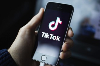 Person holding a phone showing the TikTok logo against a dark background