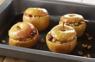 Homemade oven baked apples stuffed with pumpkin seeds and almond nuts in baking pan closeup