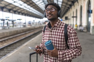 Traveler with headphones and backpack holding smartphone and reusable coffee cup is waiting for
