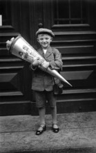 Boy with school cone, 1920s, A boy holds a large school cone in front of a door and smiles