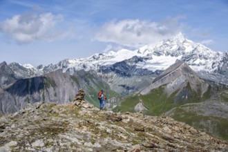 Female mountaineer on hiking trail with cairn, behind glaciated and snow-covered summit of the