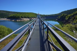 Metal footbridge over a large water reservoir, surrounded by green landscape, summer, Urft dam